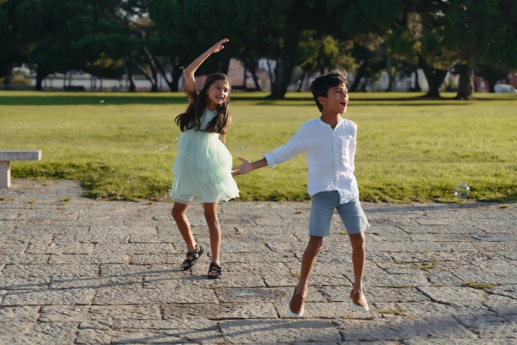 Brother and sister laughing and playing with bubbles in a scenic park in Lisbon, Portugal.