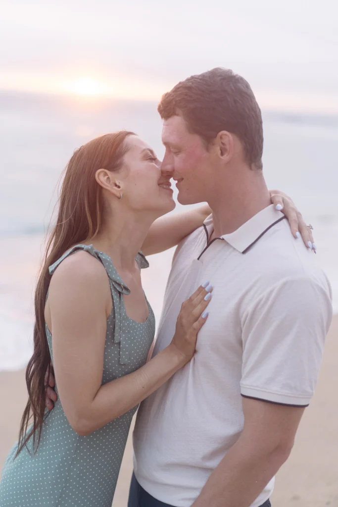 A couple leans in for a romantic kiss with the ocean and a dreamy sunset in the background. A tender moment full of love and anticipation. in ericeira