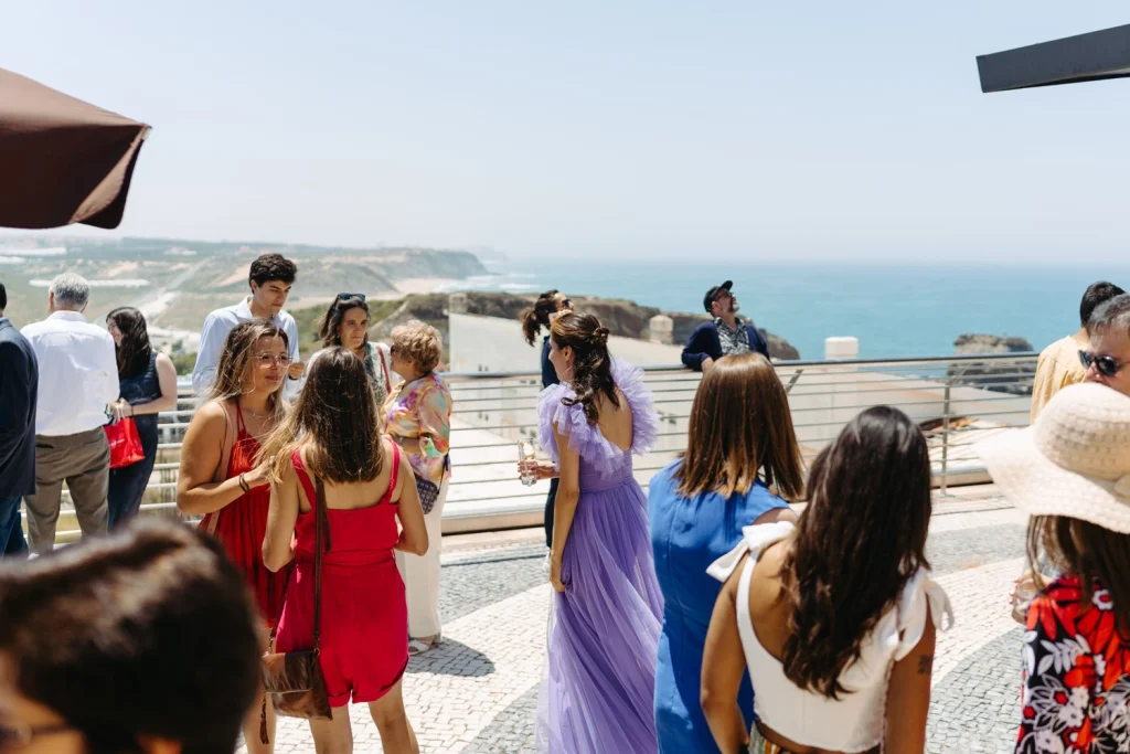 Guests mingling and enjoying the sunshine at an elegant outdoor celebration with a breathtaking coastal backdrop.
