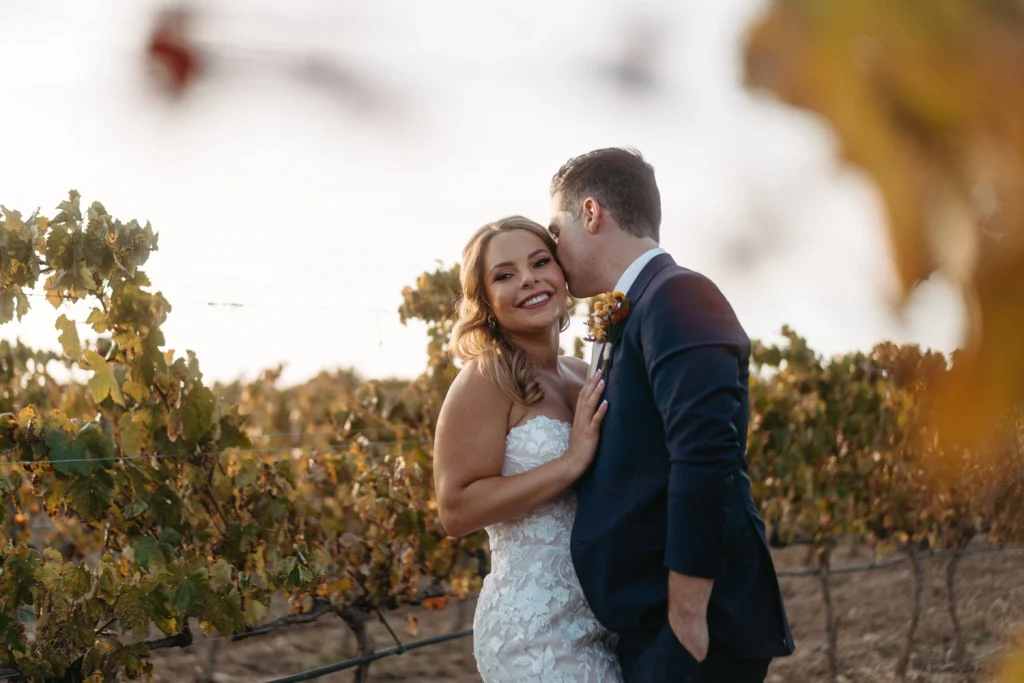 Bride and groom share a loving embrace in a vineyard, surrounded by golden leaves and warm evening light in algarve