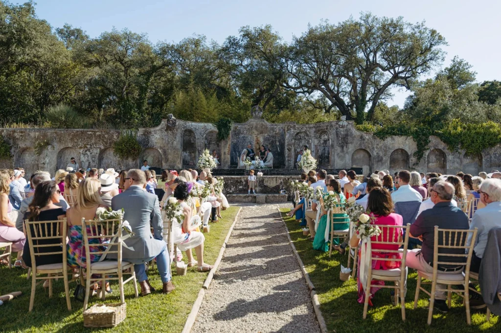 A beautiful outdoor wedding ceremony with the bride and groom exchanging vows at a historic venue, framed by loved ones and elegant décor.
