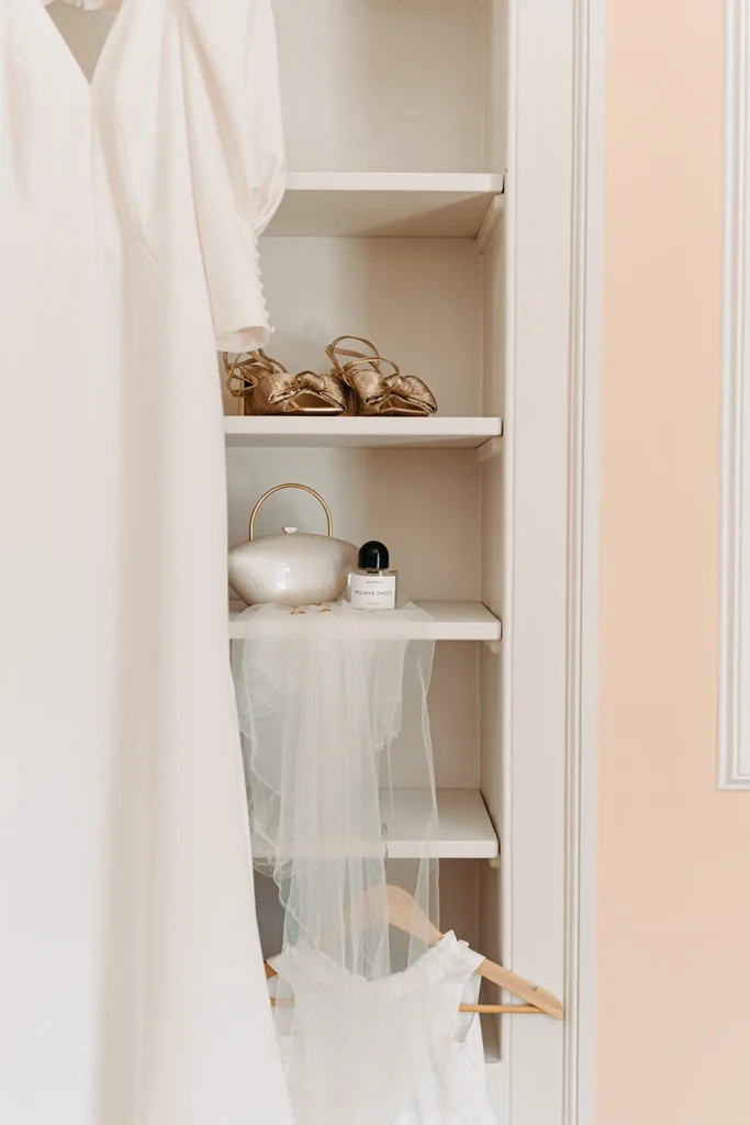 A beautiful wedding gown and bridesmaids' dresses hanging elegantly in a pastel-colored room.