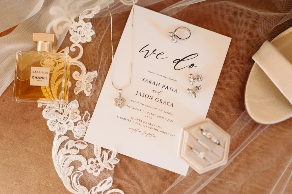 A wedding invitation flat lay featuring Chanel perfume, diamond jewelry, and delicate lace accents in quinta de santana