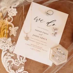 A wedding invitation flat lay featuring Chanel perfume, diamond jewelry, and delicate lace accents in quinta de santana