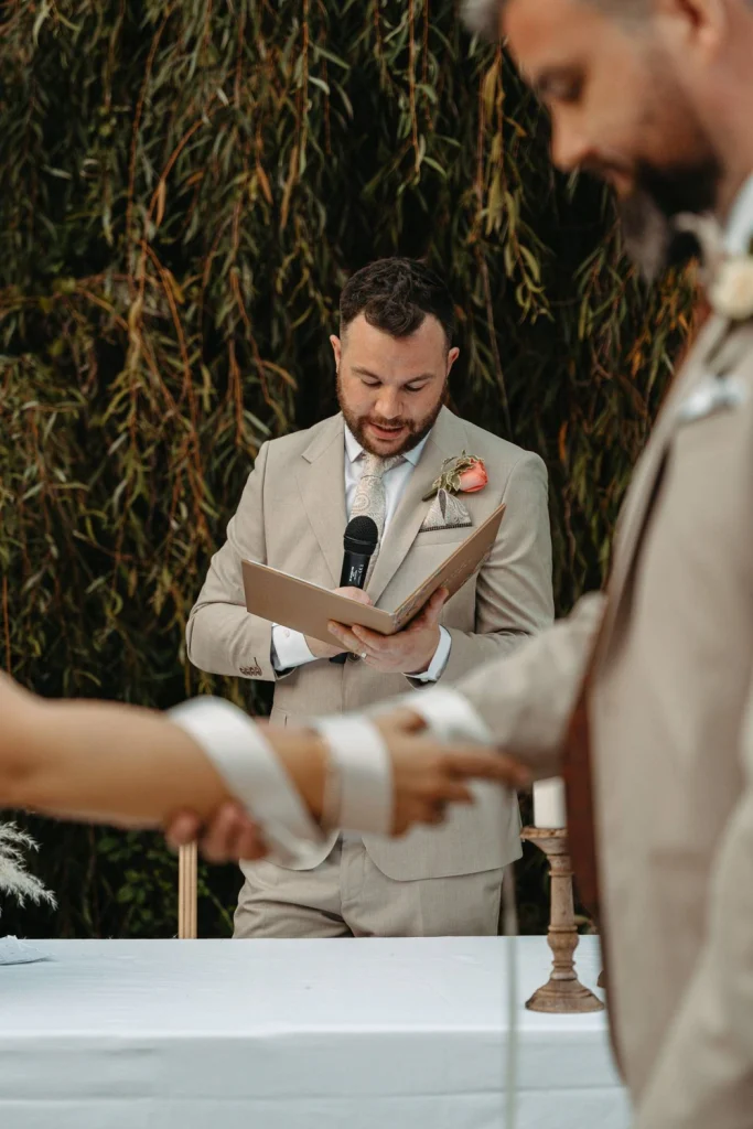 A close-up of the wedding officiant reading from a vow book as the couple holds hands during their ceremony.
