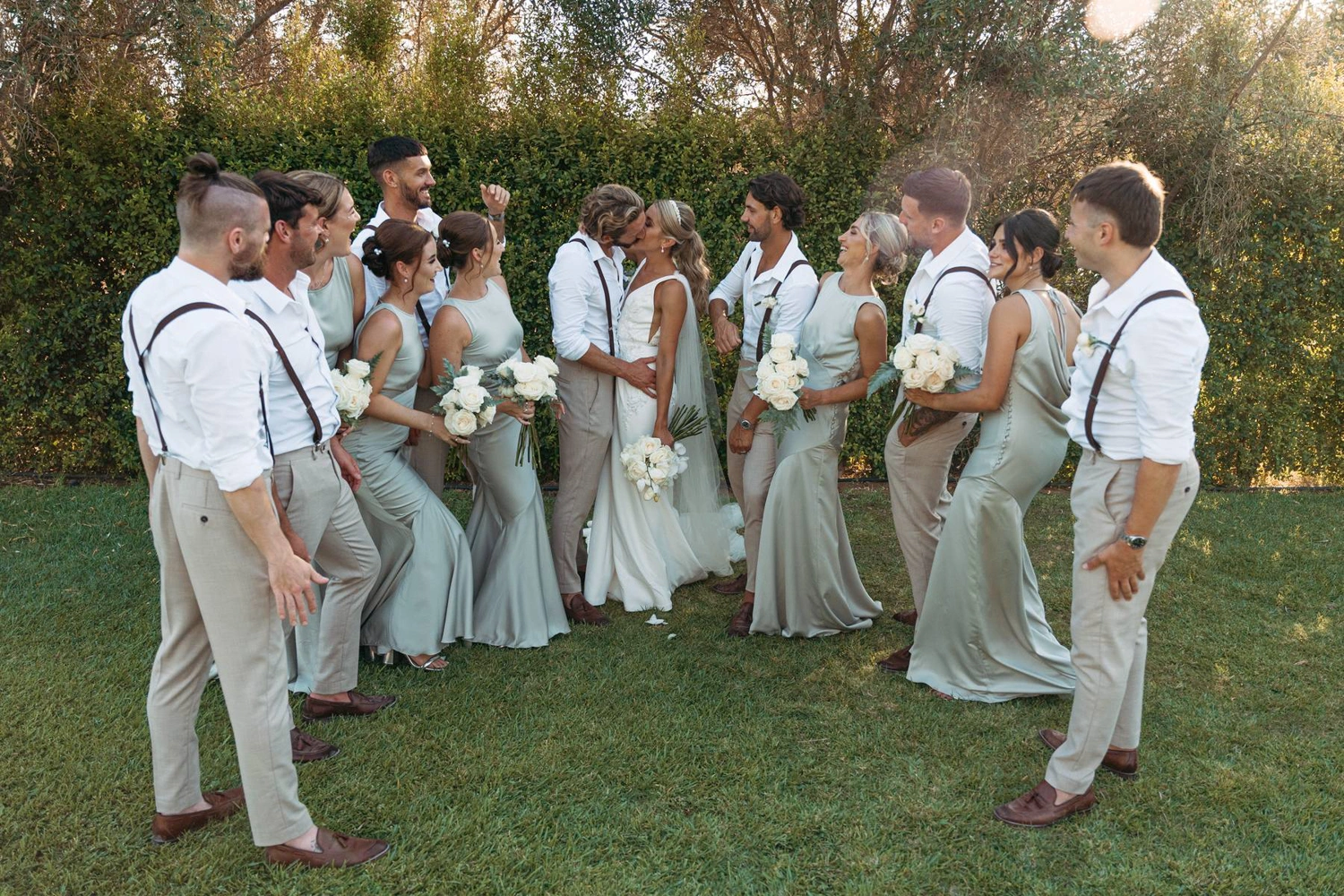 Bride and groom kissing, surrounded by bridesmaids in sage dresses and groomsmen in suspender in Algarve