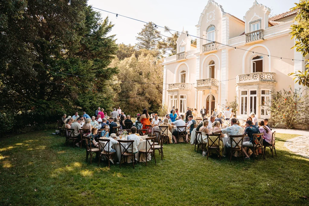 Guests enjoying an outdoor wedding reception at a historic venue with lush gardens and warm sunlight.