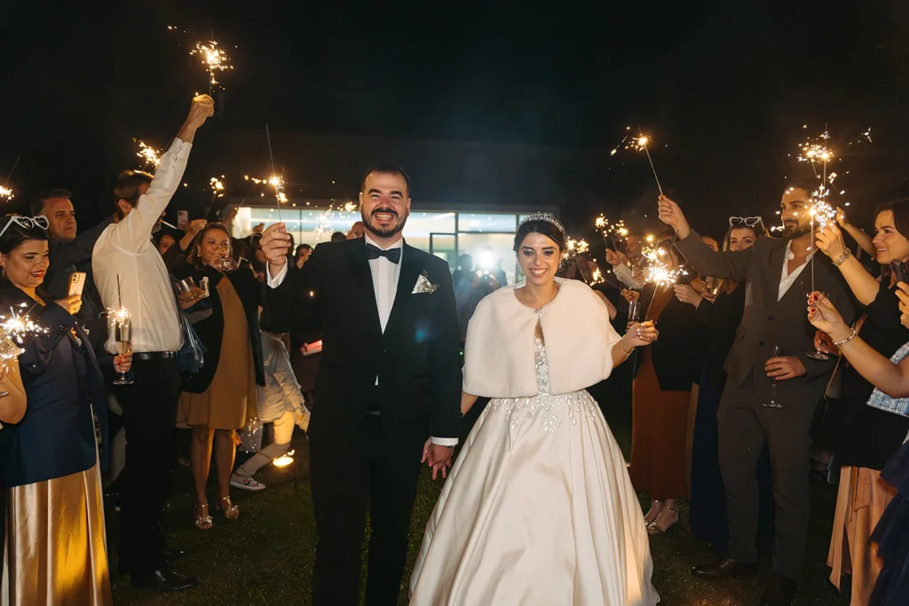 The newlyweds walk hand in hand through a glowing tunnel of sparklers, surrounded by smiling guests.