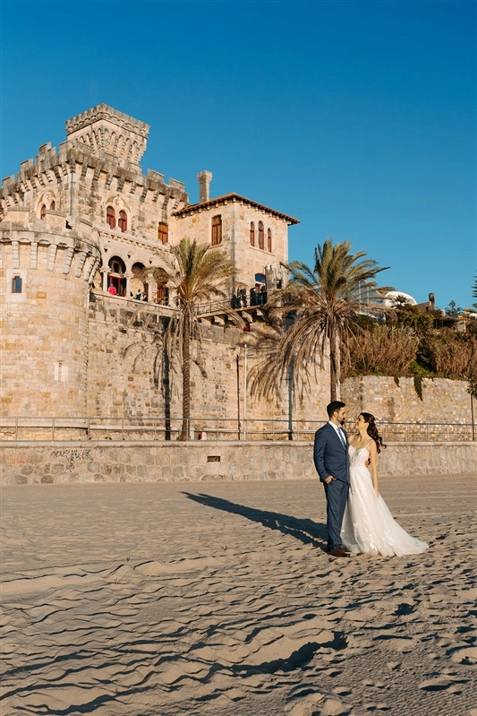 Bride and groom on the beach in front of Forte da Cruz in Estoril, Portugal.