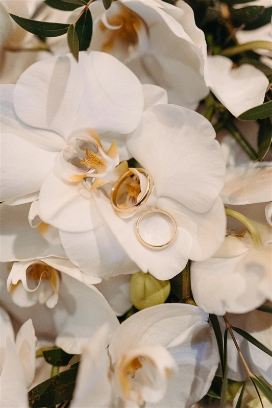Close up of gold wedding rings resting on white orchids during an elegant Lisbon wedding.